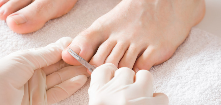Pedicurist's hands in protective rubber gloves cutting toenails with scissors.