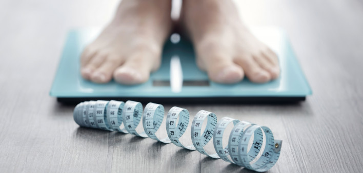 mans feet on scale with measuring tape on floor