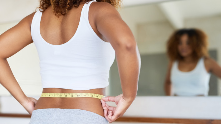 ropped shot of a young woman measuring her waist in the bathroom