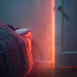 A depiction of a house fire, indoors. Smoke and light from a fire pour through a cracked room door, a person visible sleeping in their bed. Horizontal with copy space.