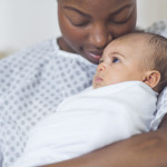 Beautiful African American mother in a hospital gown holds her newborn baby