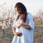 Portrait of a beautiful, young African woman enjoying her pregnancy at the orchard in bloom.