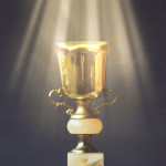 Golden trophy on pile of books, against blackboard, with sun rays over trophy; learning/achievement