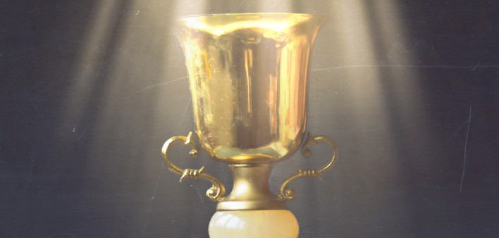 Golden trophy on pile of books, against blackboard, with sun rays over trophy; learning/achievement