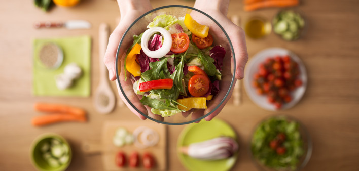Hands holding an healthy fresh vegetarian salad in a bowl, fresh raw vegetables on background