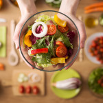 Hands holding an healthy fresh vegetarian salad in a bowl, fresh raw vegetables on background