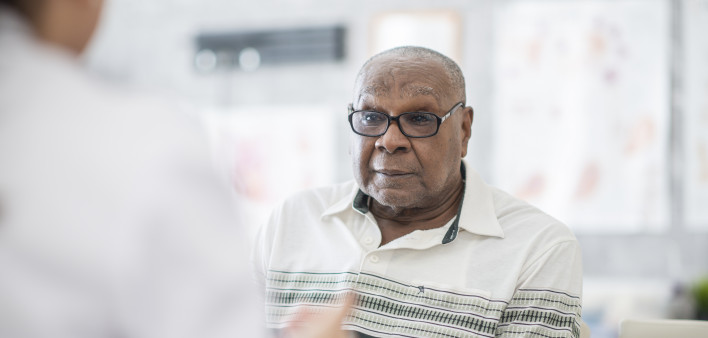 An African American man wearing eyeglasses sits in a doctor's office