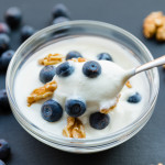bowl of yogurt and blueberries with walnuts and a spoon