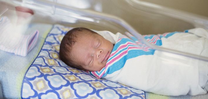 Sleeping baby boy resting in a hospital crib in a hospital delivery room.