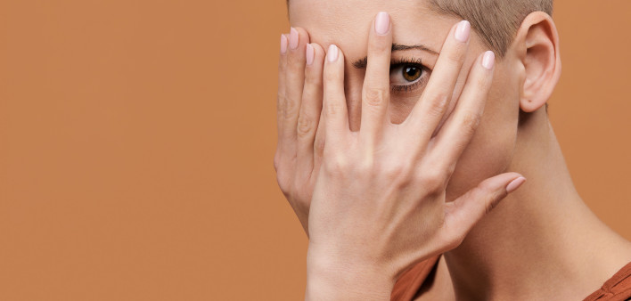 Beautiful young woman with shaved head covering her face with both hands