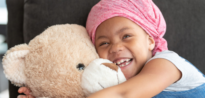 Happy girl with cancer hugs large teddy bear