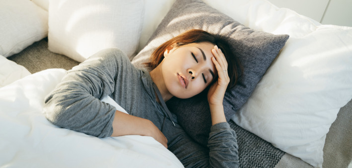 Young Asian woman with hand on forehead lying in bed and feeling sick