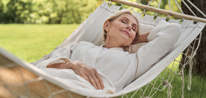 Smiling beautiful woman is having rest in green yard in open air on sunny warm day