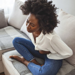 woman lying on her sofa alone and suffering from period cramps