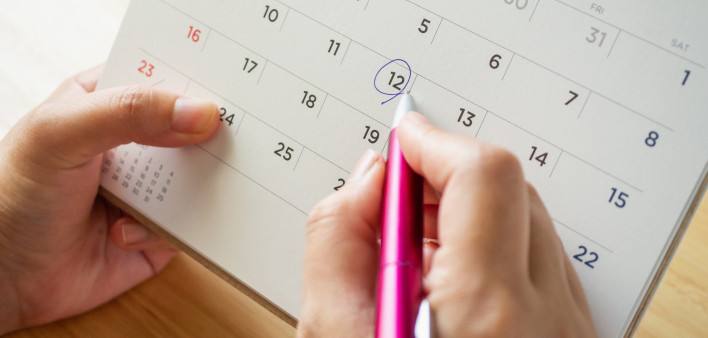 Calendar page with female hand holding pen on desk table