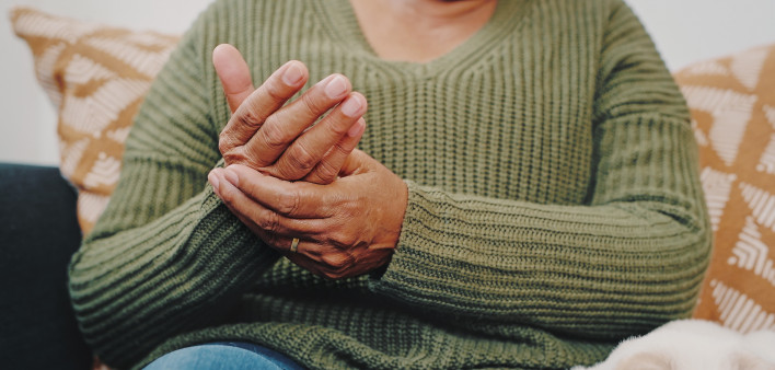 Cropped shot of an unrecognizable senior woman rubbing her hands while sitting on the sofa in her apartment with her cat beside her