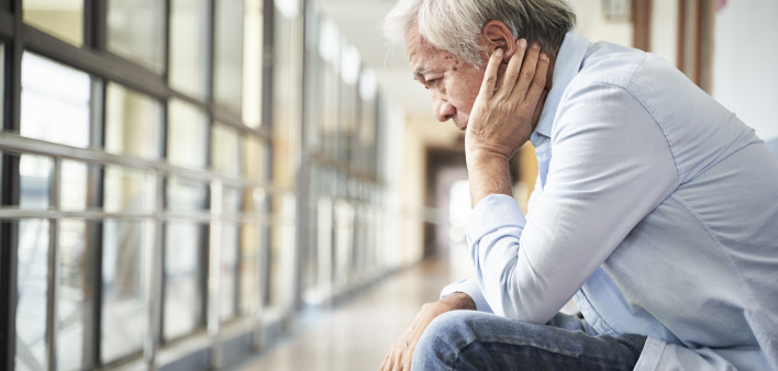 senior asian patient sitting in hospital hallway looking sad and depressed