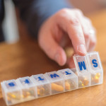 mans finger with pill box and glass of water
