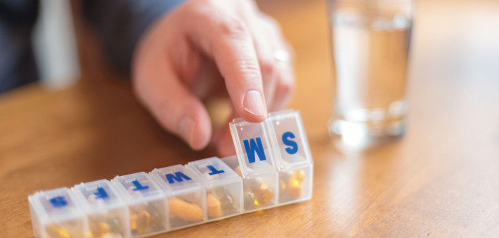 mans finger with pill box and glass of water