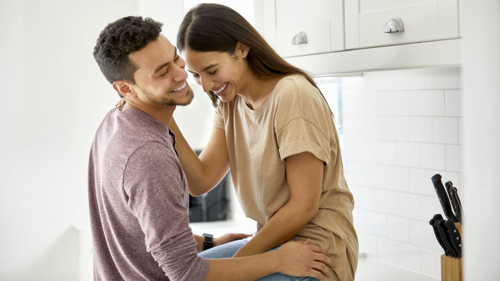 Cheerful Latino young couple talking in kitchen at home