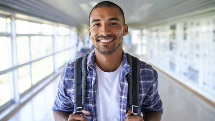 Portrait of a happy young man standing in a corridor on campus