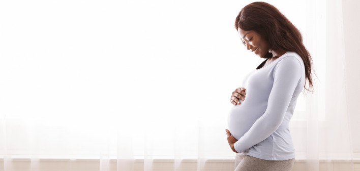 Beautiful pregnant afro woman hugging her tummy,