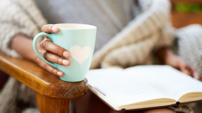 woman holding coffe cup with heart and heading a book