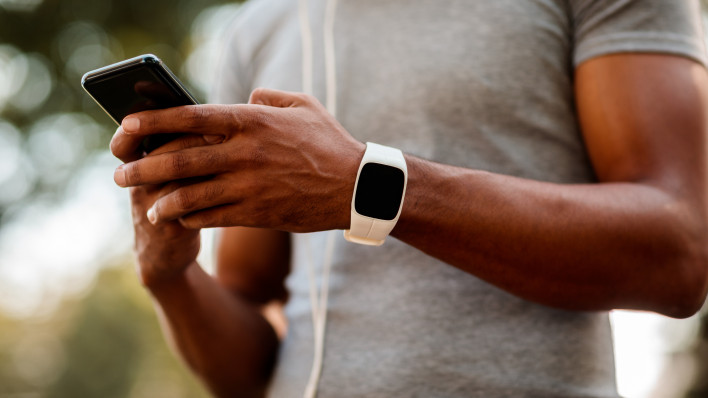African-American male with smart watch and headphones texting messages on mobile phone during jogging session.