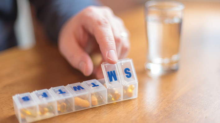 mans finger with pill box and glass of water