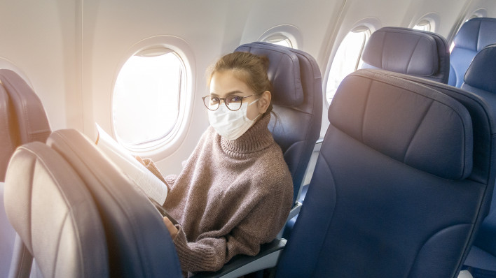 A young woman wearing face mask is traveling on airplane , New normal travel after covid-19 pandemic
