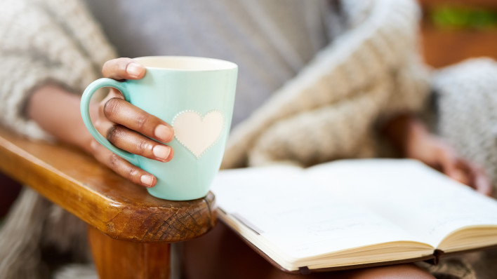 woman holding coffe cup with heart and heading a book
