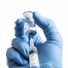 hand in blue gloves holding vial and syringe