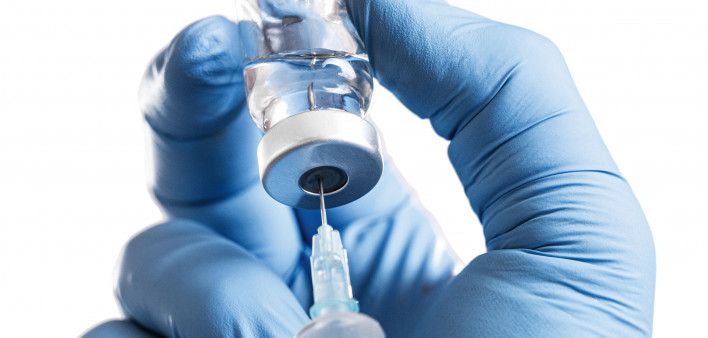 hand in blue gloves holding vial and syringe