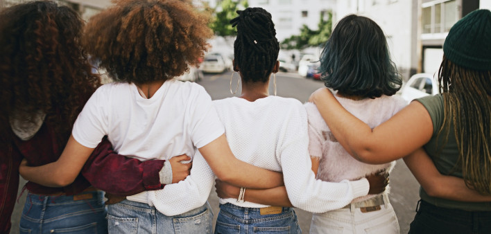 Rearview shot of a group of unrecognizable young friends walking with their arms around each other in the city
