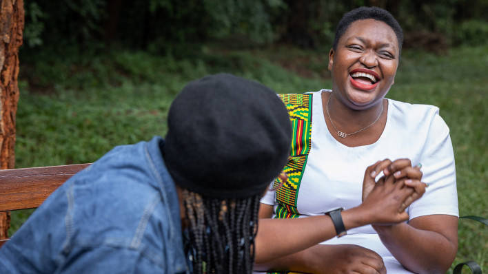 Two friends enjoying a laughing while having a conversation on a park bench in Nairobi, Kenya, the woman on the right is living with HIV