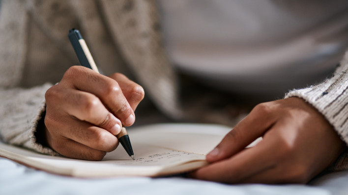 Cropped shot of a man writing in a notebook on his bed at home