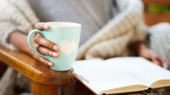 woman holding coffe cup with heart and heading a book
