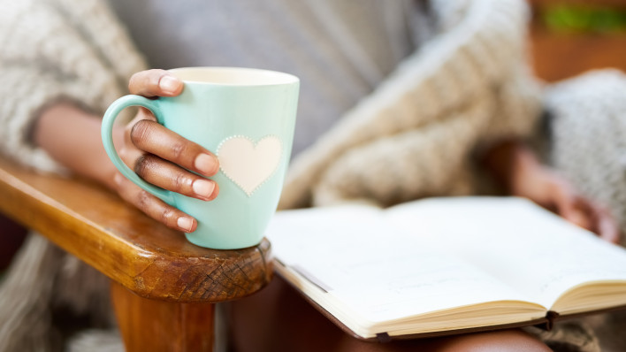 woman holding coffe cup with heart and heading a book