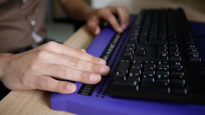 Blind person using computer with braille computer display and a computer keyboard.