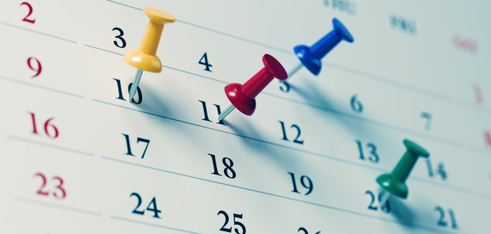 White calendar with colored push pins reminding important dates