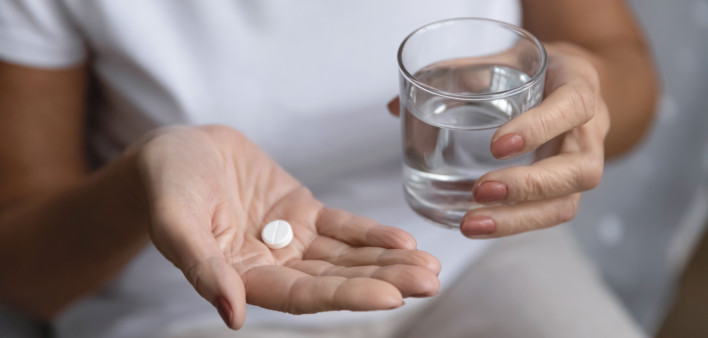 hands holding pill and glass of water