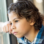 Pensive hispanic little boy looking through a window