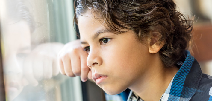 Pensive hispanic little boy looking through a window