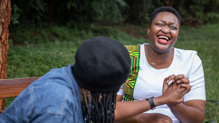 Two friends enjoying a laughing while having a conversation on a park bench in Nairobi, Kenya, the woman on the right is living with HIV