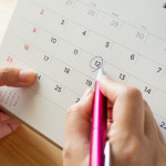 Calendar page with female hand holding pen on desk table