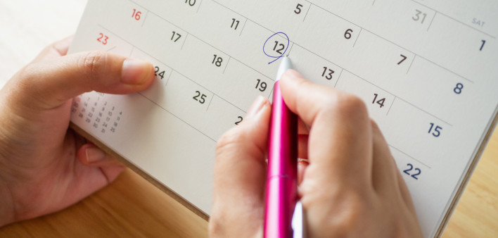 Calendar page with female hand holding pen on desk table