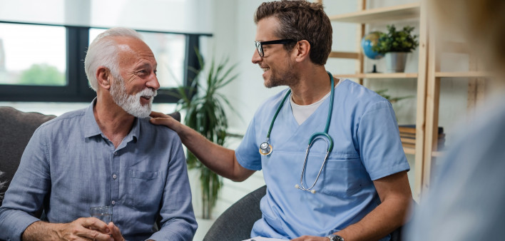 Happy doctor talking to senior male patient while being in a home visit.