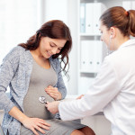 pregnancy, gynecology, medicine, health care and people concept - gynecologist doctor with stethoscope listening to pregnant woman baby heartbeat