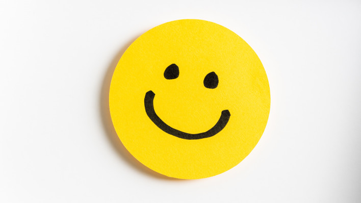 Drawing of a happy smiling emoticon on a yellow paper and white background.