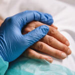 doctor hand with blue glove giving support and love to a patient at hospital. Coronavirus
